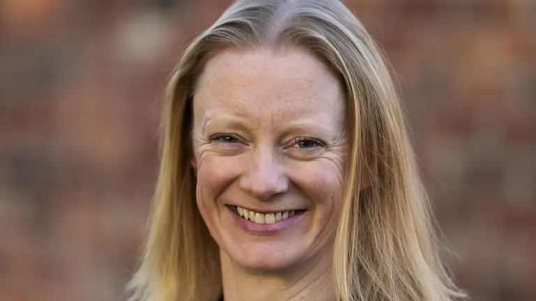 Blonde woman with a smile, wearing a blue top and black blazer.
