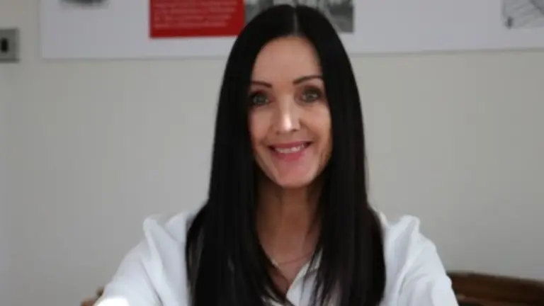 Woman with long black hair smiling at the camera while seated at a desk.