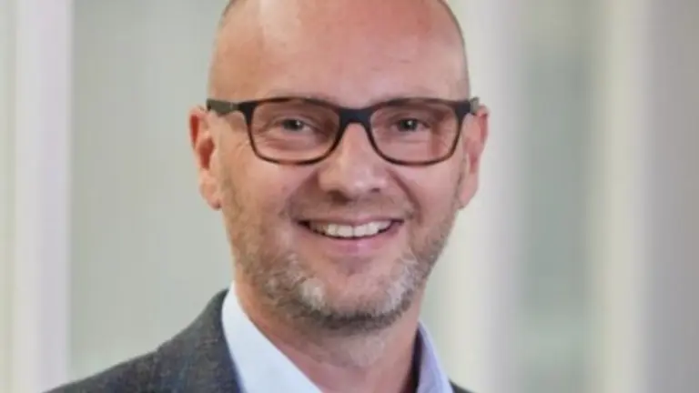Bald man in glasses and a blue shirt smiling at the camera.