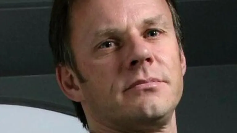 Man with brown hair, wearing a black shirt, with a serious expression.