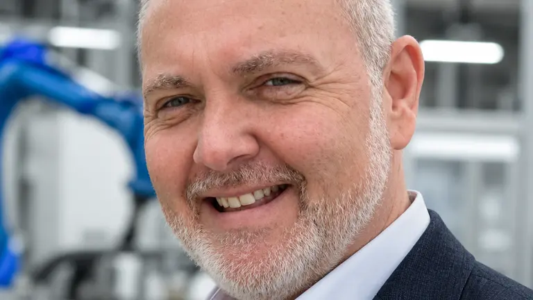 Man in a suit smiling inside a factory.