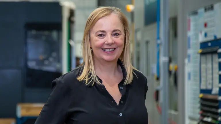 A smiling woman with blonde hair wearing a black shirt in a factory.