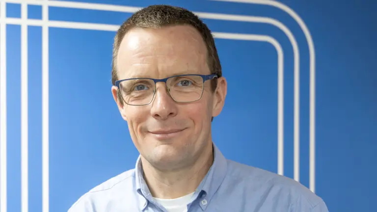 Man with glasses smiling against blue background with white lines