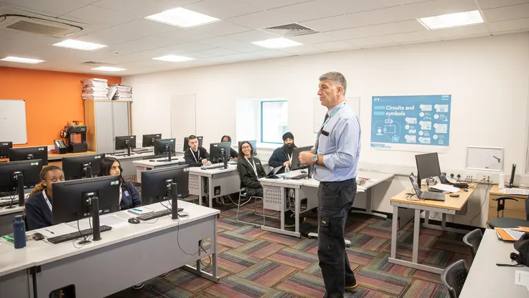 A man giving a lecture in a computer classroom.
