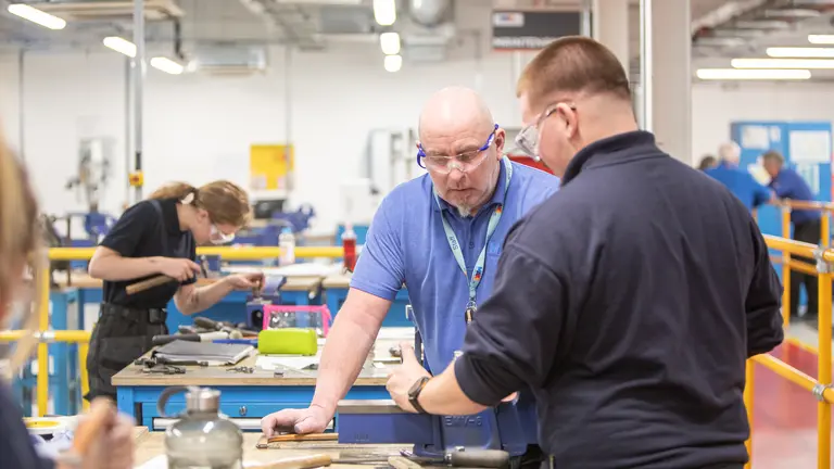 Tutor and apprentice examine objects on a table.