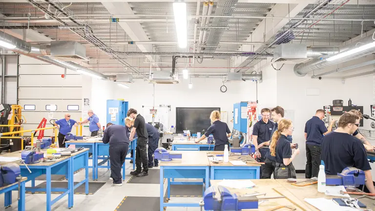 A group of people working on blue work tables in a factory.