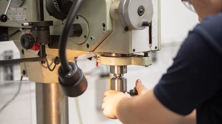 Worker using a drill press to drill a piece of metal.