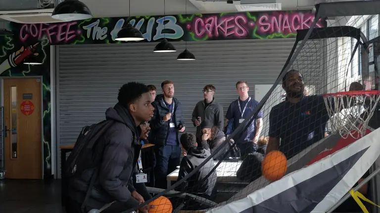 Apprentices in a break room with two people playing basketball.