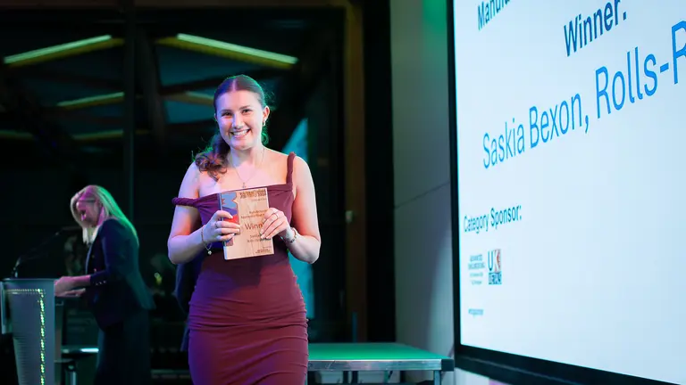 Woman holding award, standing in front of large screen with "Winner: Saskia" displayed.