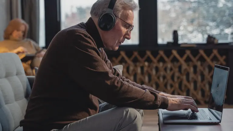an older man with headphones on sitting forward engaged with his laptop