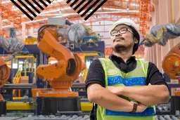 Man standing with three robotic arms behind him in a manufacturing setting