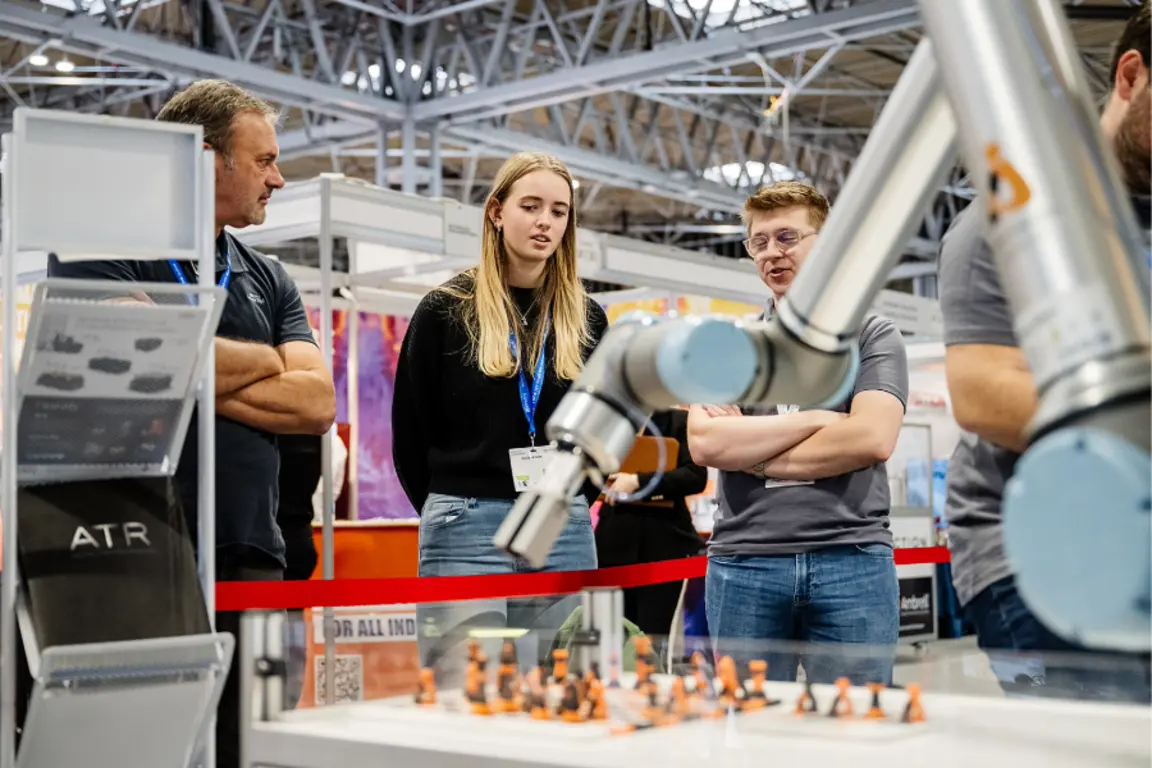 Image of three people in a factory watching a robot create a product