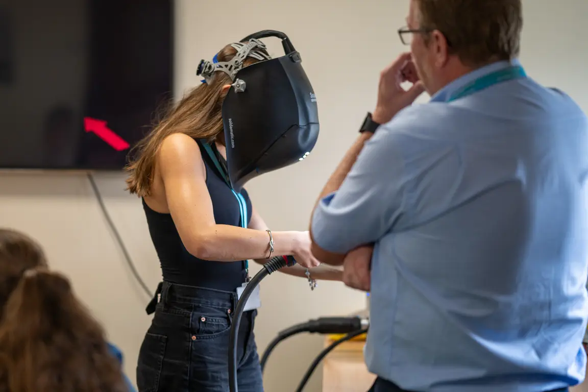A person welding while an instructor stands nearby observing the activity.