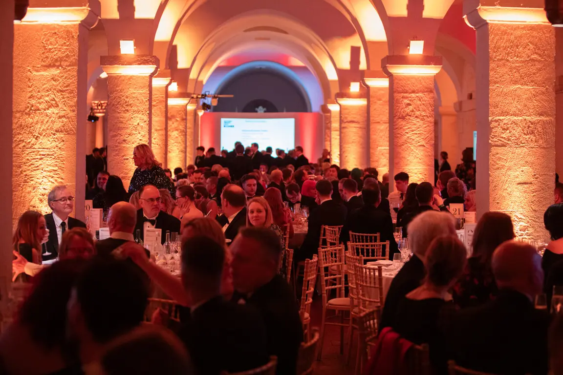Large room with arched columns illuminated by warm lights, filled with seated guests.