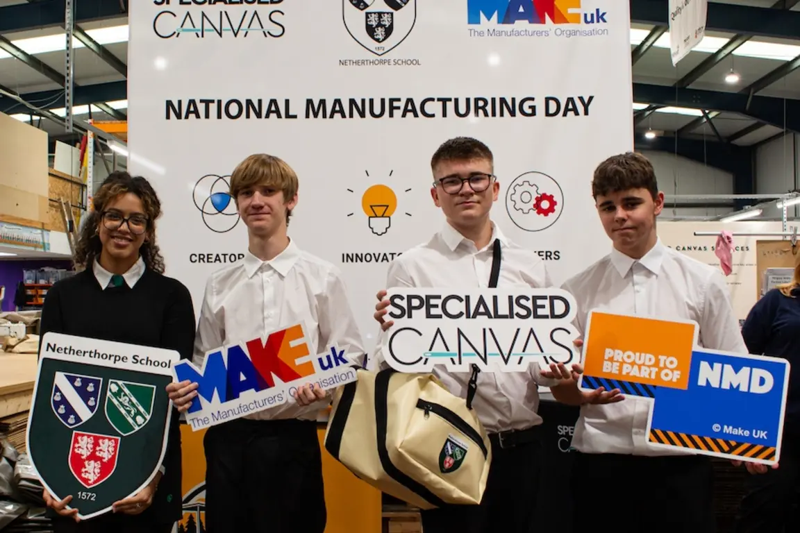 Four students pose with signs for Specialized Canvas and National Manufacturing Day.