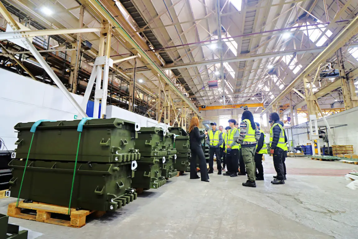 During NMD Several people wearing safety vests view large green military containers in a warehouse.