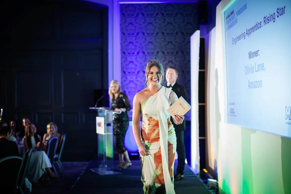 Woman in a white dress walks across the stage at an awards ceremony.