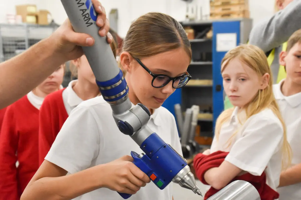 Girl using robotic arm to drill a hole in a metal plate on NMD.