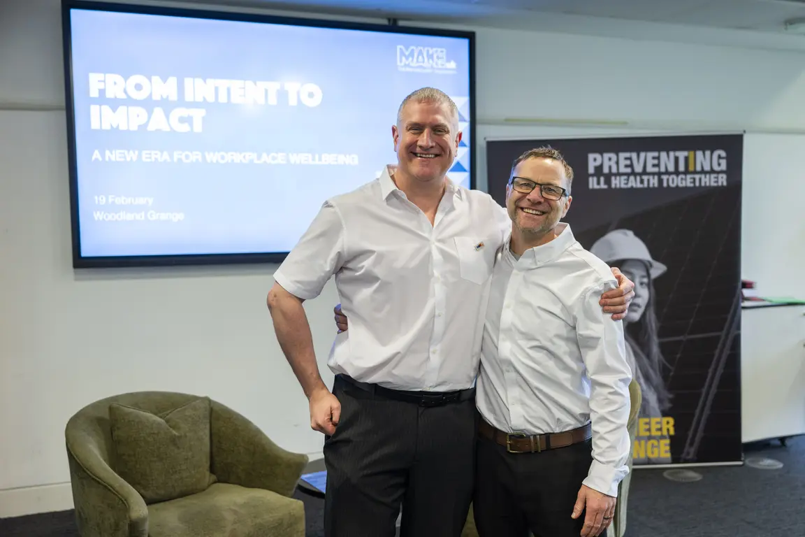 Two men stand next to a poster with the words "From Intent to Impact".