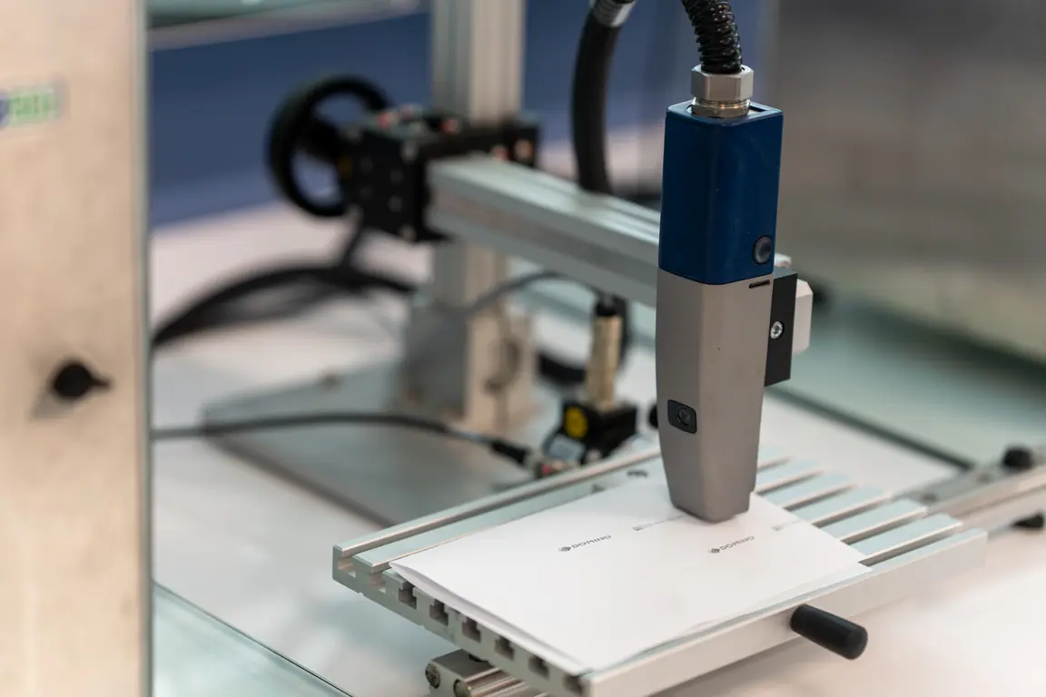 Blue and silver robot arm pressing a label onto a white sheet.