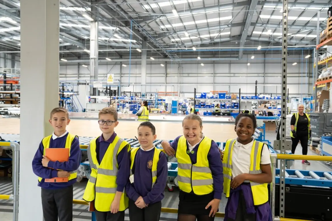 Five children in yellow safety vests pose for a picture in an industrial setting for National Manufacturing Day.