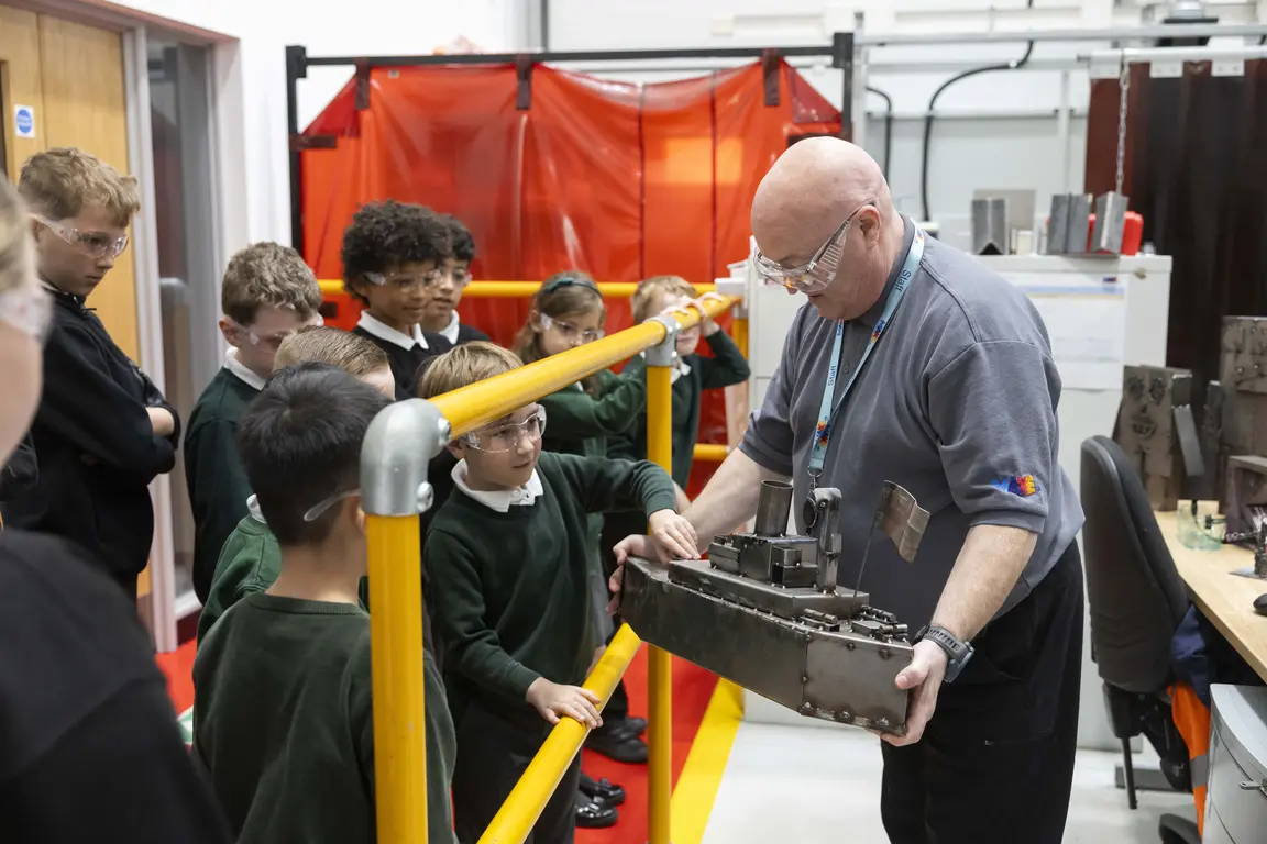 Man with glasses holding an engine part while children look on.