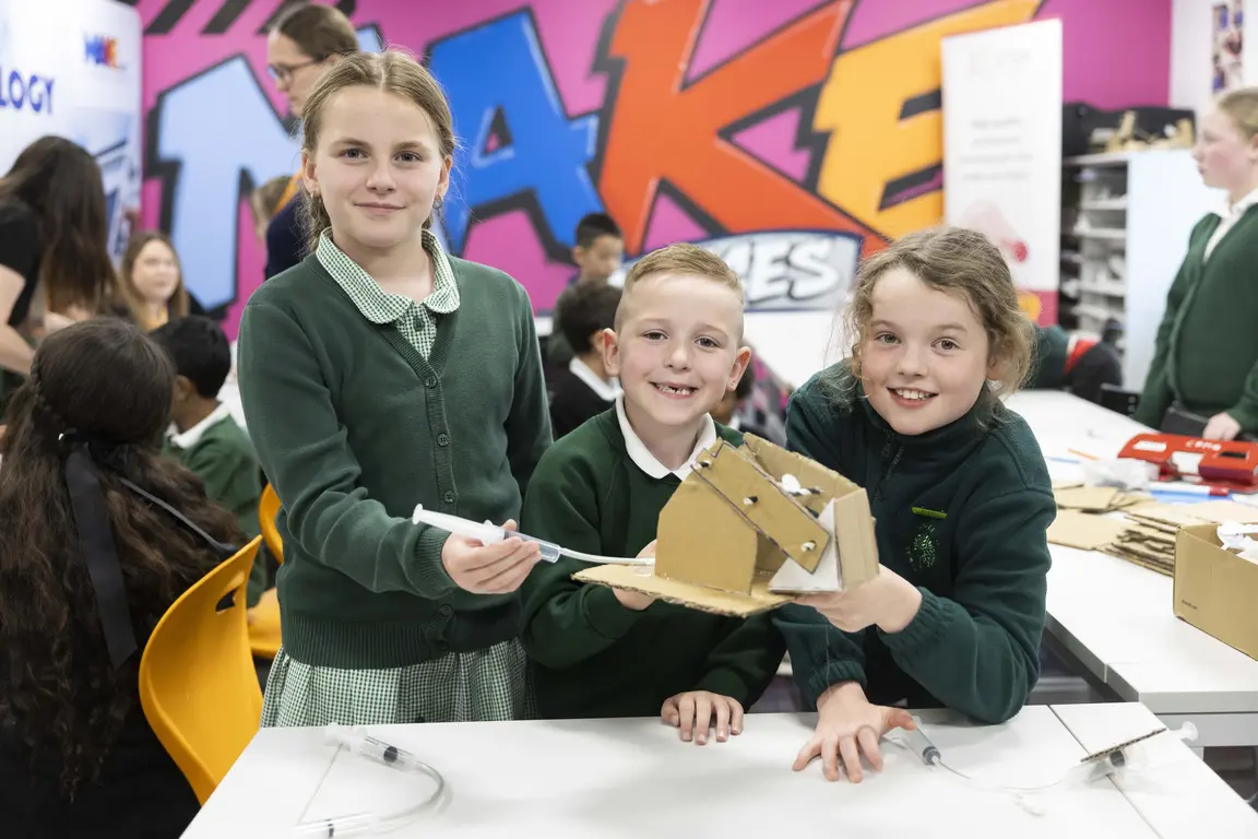Thrree Primary School Aged Children (order: girl, boy, girl) hold model mechanical arm they've created