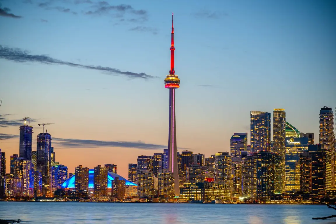 Toronto city skyline at dusk with a tall tower and red lights.