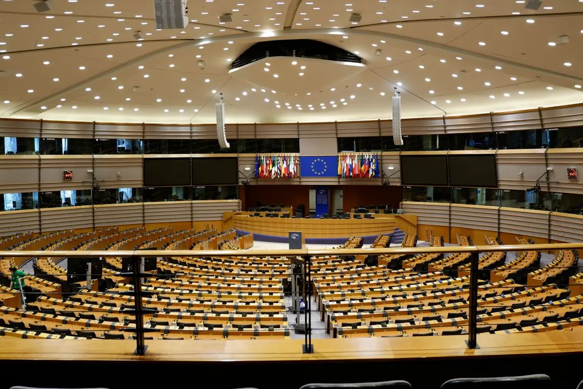 An empty European Parliament chamber with flags displayed on a stage.