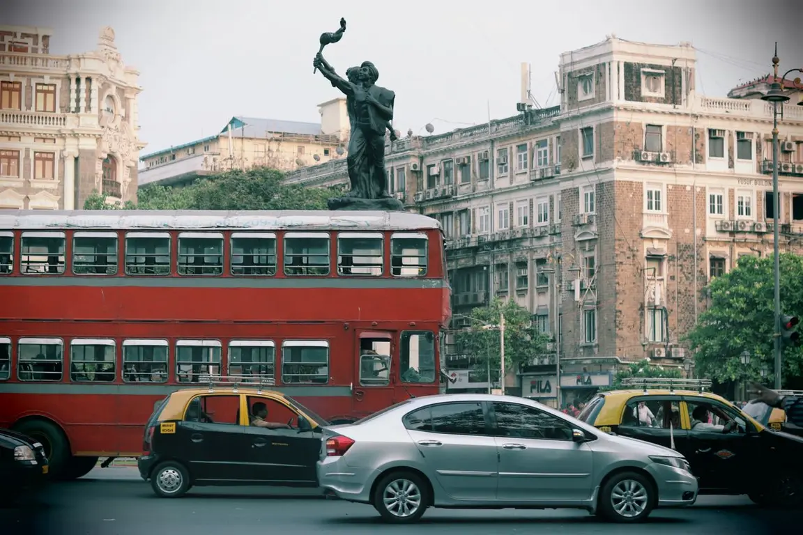A red double-decker bus with a statue on top is stopped in the middle of traffic.