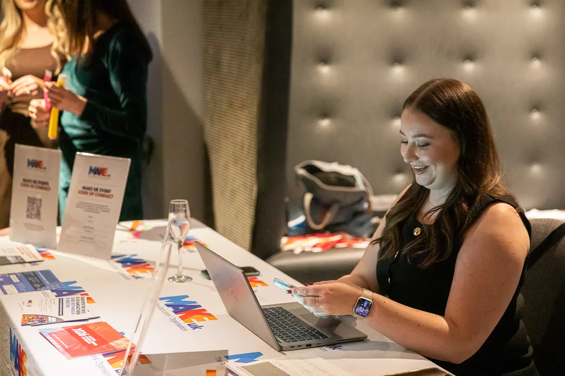 Woman seated at a table with a laptop and smiling.