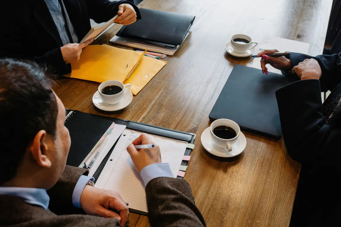 Business meeting with three people and one taking notes on a notepad