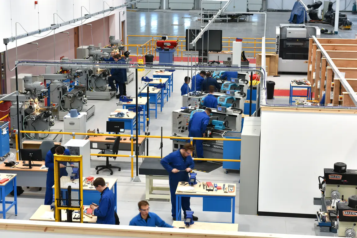 Factory floor with workers in blue uniforms operating various machines.