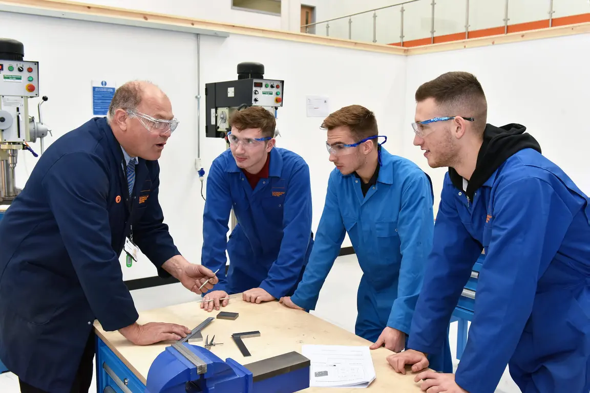 Five men in blue coats and safety glasses working in an engineering lab.