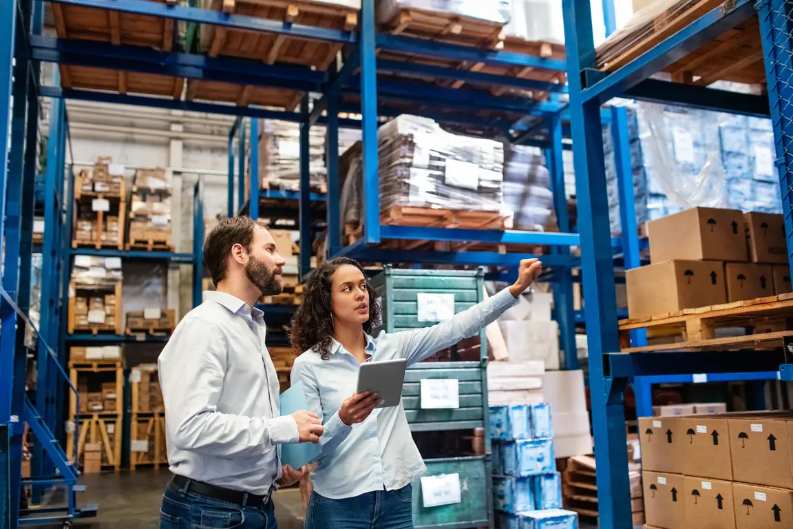 Two adults in a warehouse looking at a tablet.