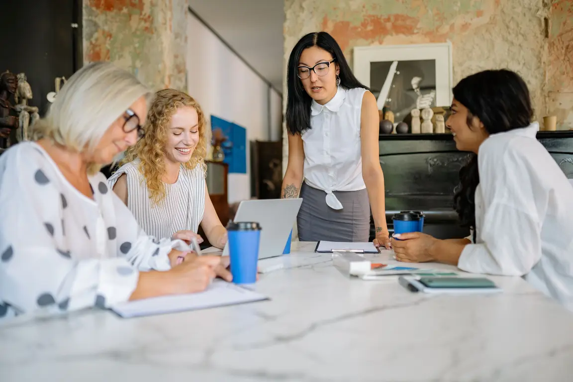 Four women in a meeting discussing work at a table.