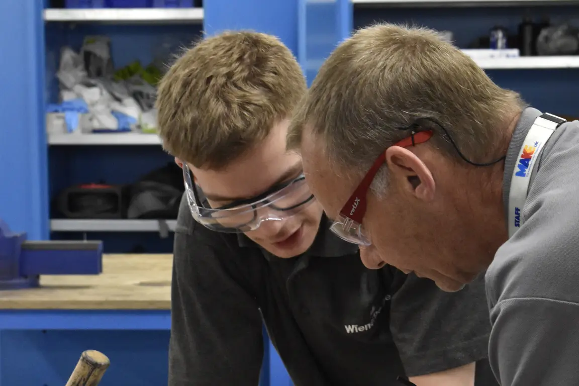 Tutor teaching apprentice at workbench