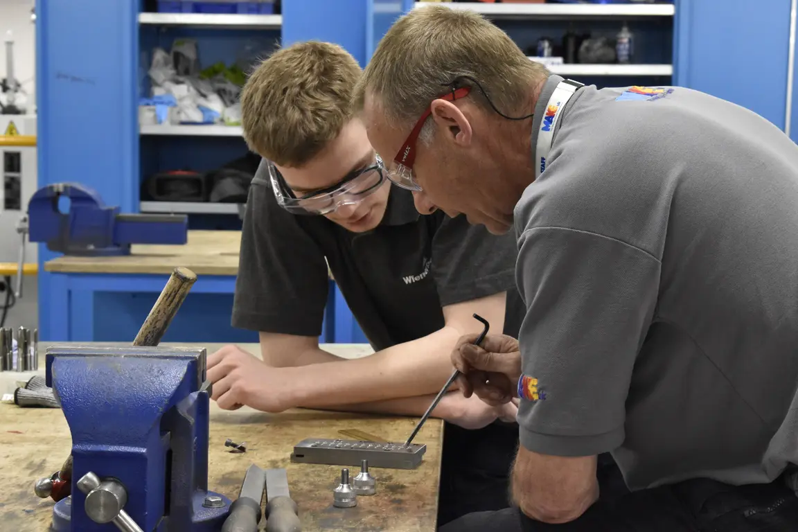 Tutor teaching apprentice at workbench