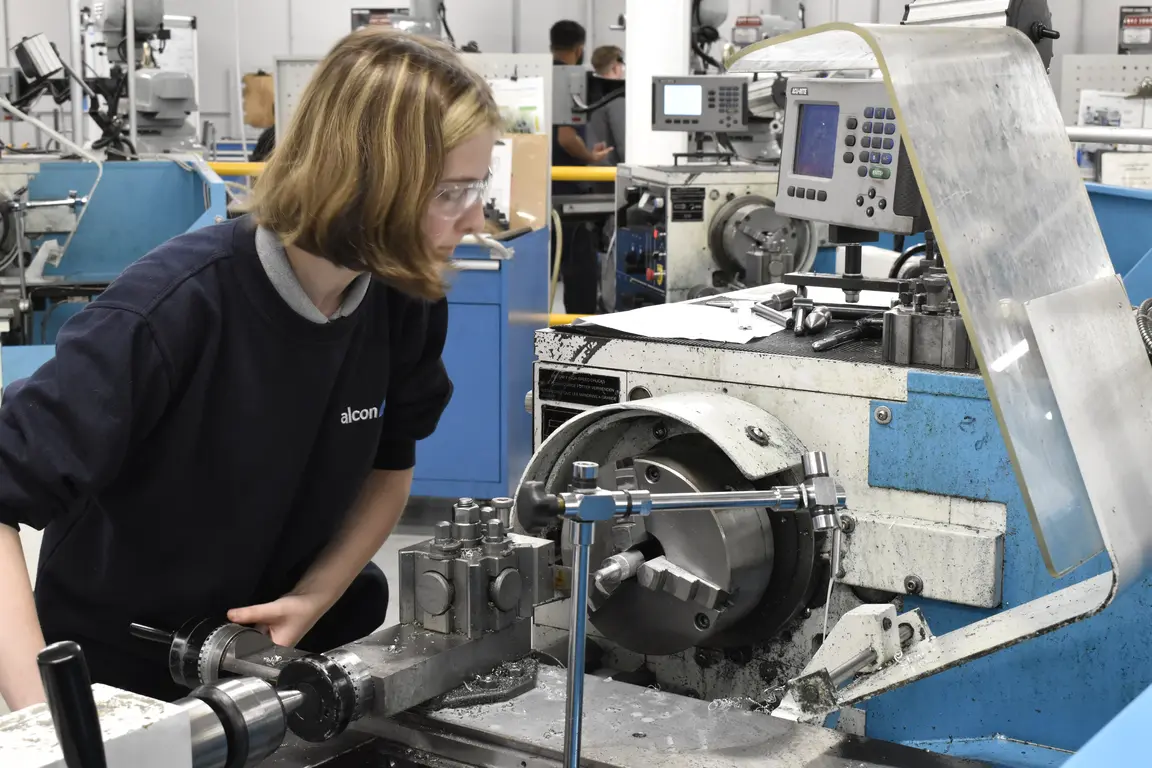 A woman wearing safety goggles works on a machine in a factory.