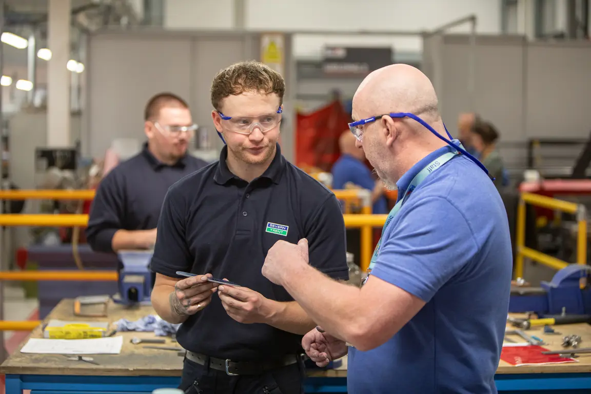 Two men in a factory talking about a part they are holding
