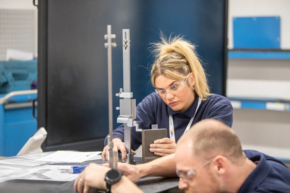 apprentices with glasses work together on a device in a lab