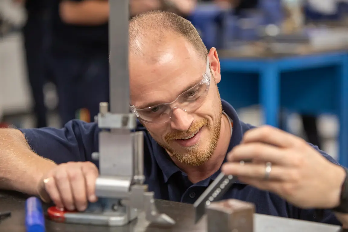 Apprentice wearing safety glasses and a blue shirt working on a metal press.