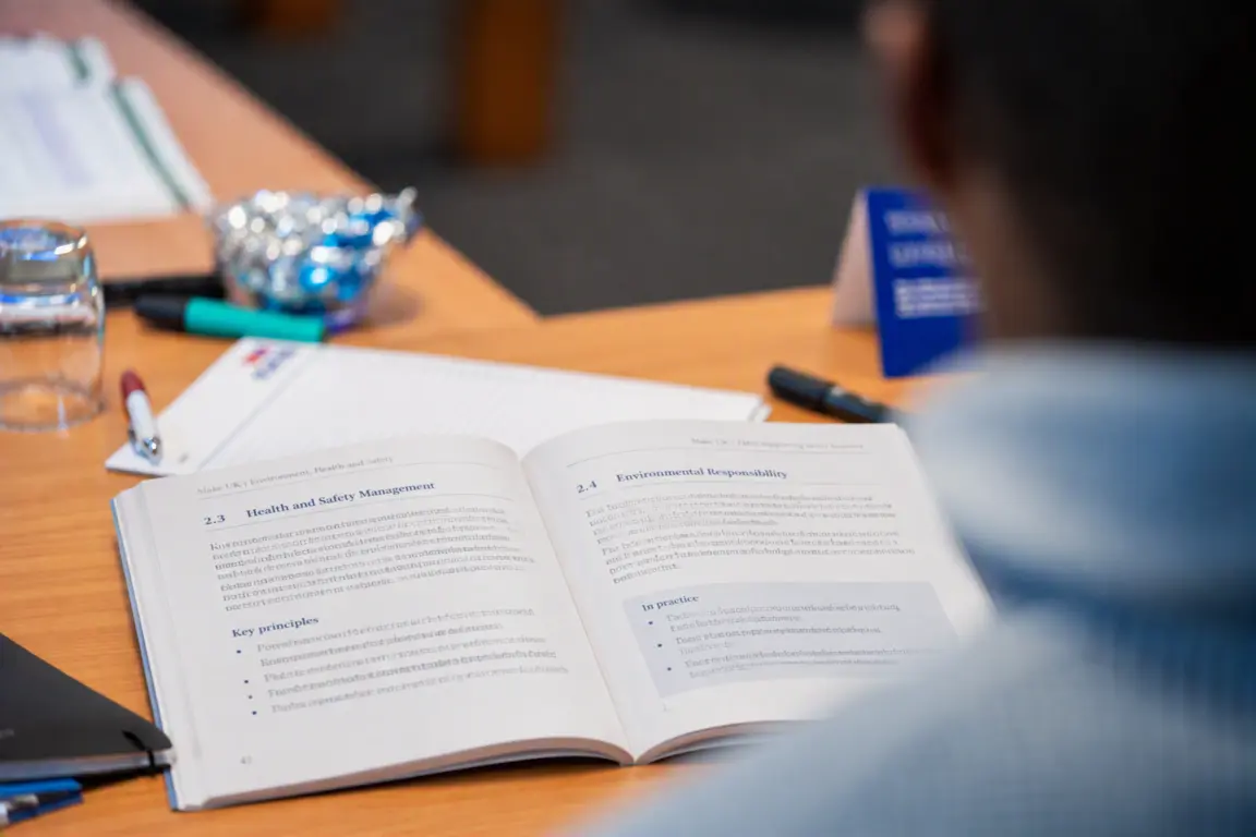Person reading a blue and white open book at a conference.