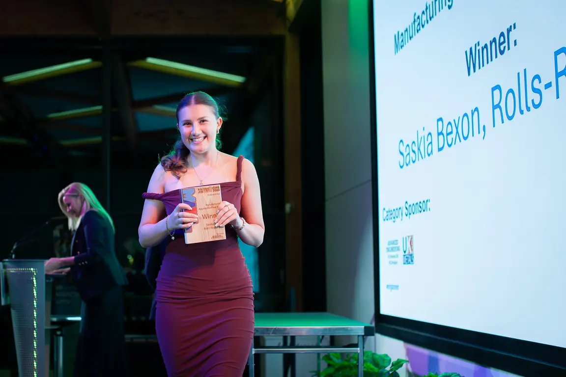 Woman holding award, standing in front of large screen with "Winner: Saskia" displayed.