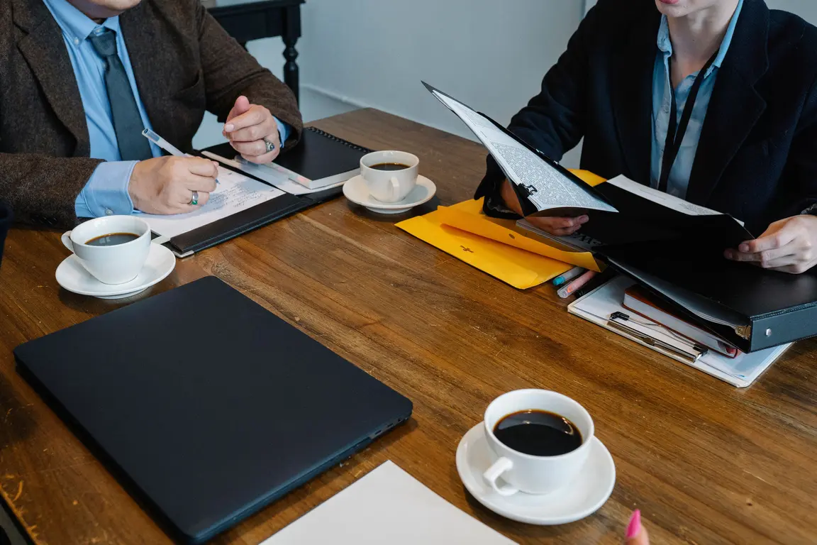 Two people in a meeting with papers and coffee on a desk.