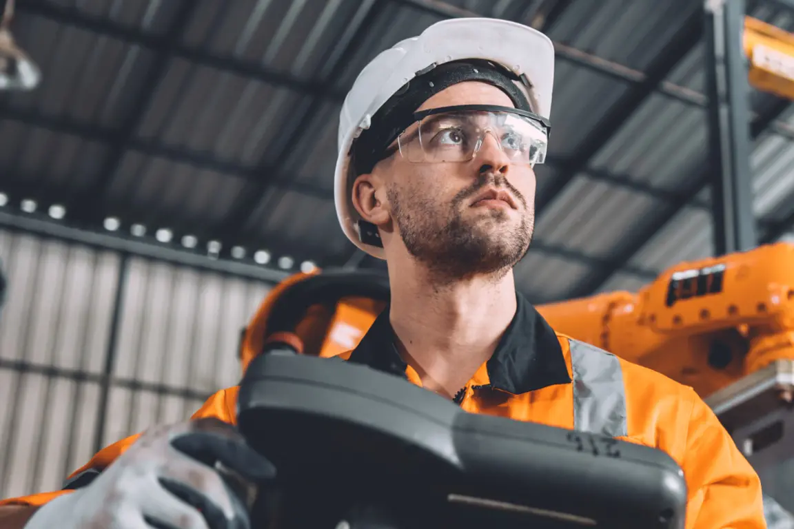 Industrial operator in orange hi-vis gear handling heavy machinery with precision, exemplifying CDM safety standards in an engineering environment