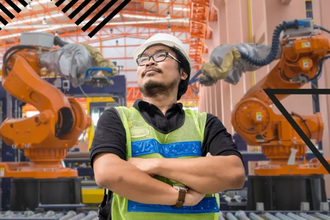 Man standing with three robotic arms behind him in a manufacturing setting