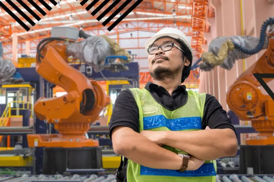 Man standing with three robotic arms behind him in a manufacturing setting