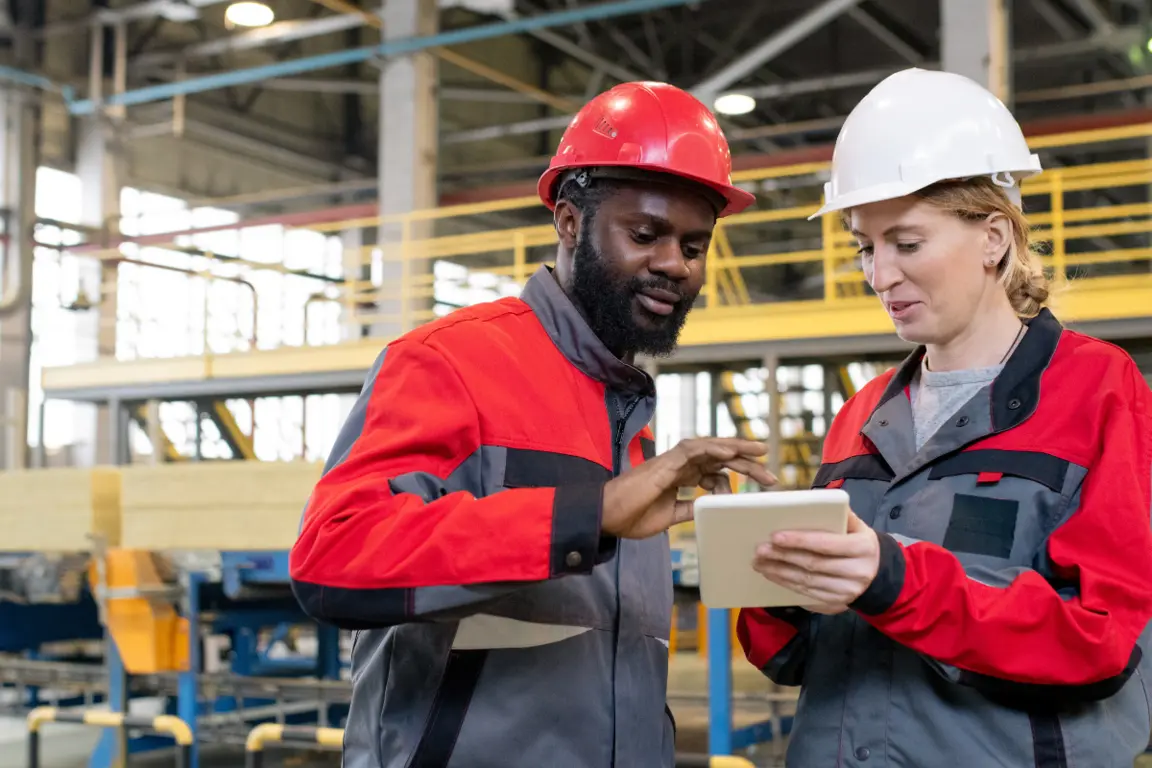 Diverse team of construction professionals with tablet in factory setting, engaging in CDM-focused planning and risk assessment discussion