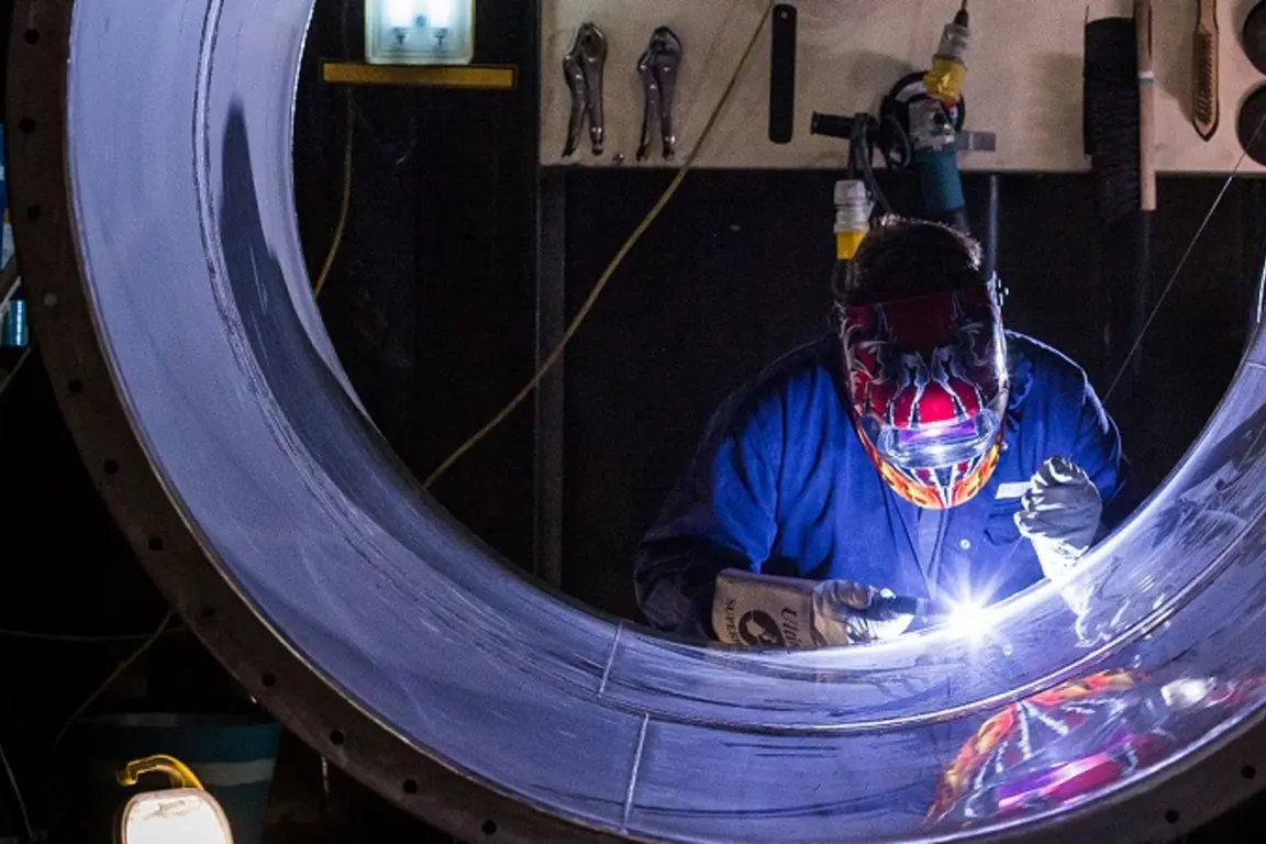 Worker welding a pipe in a dark room.